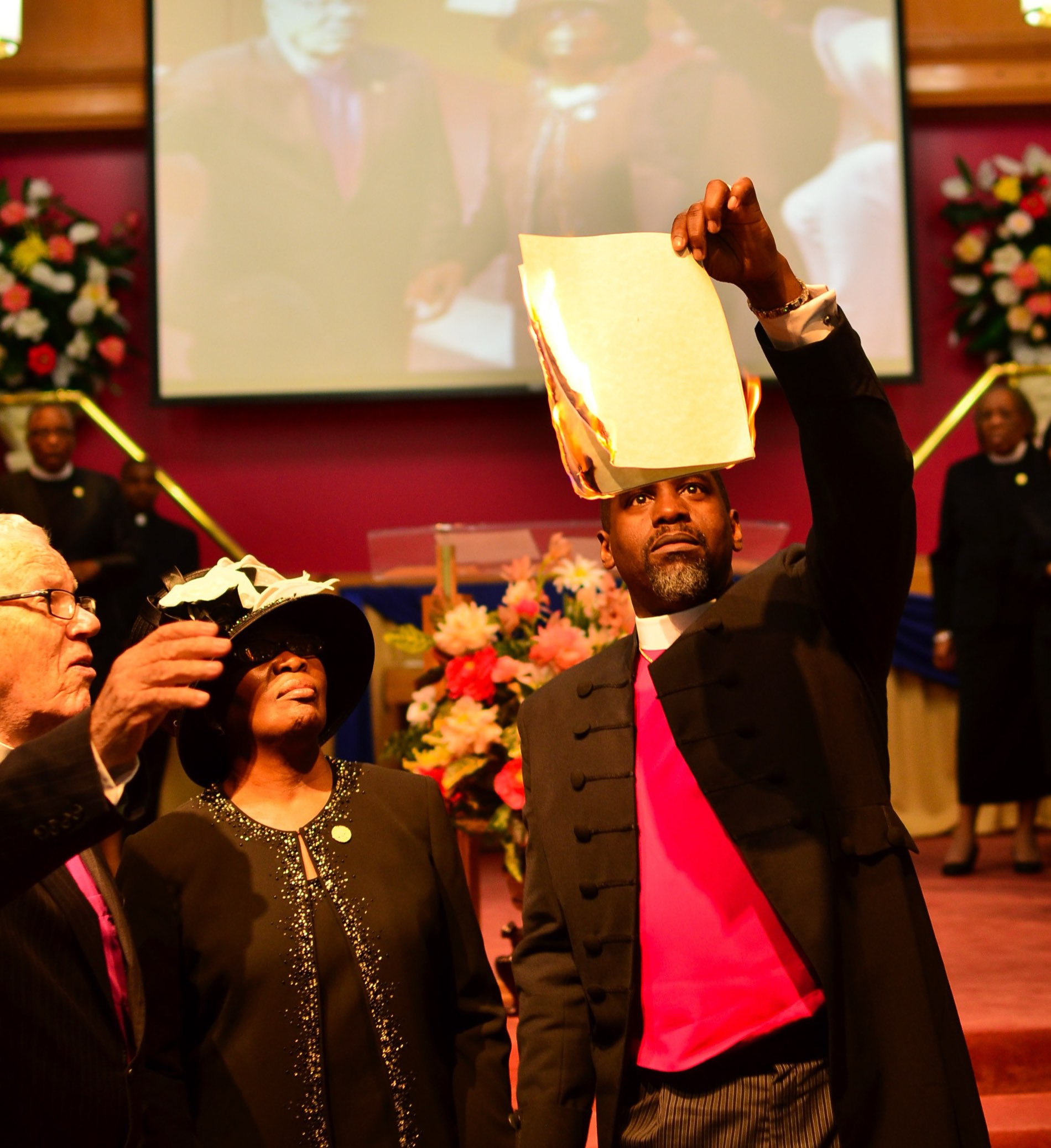 During a celebration service, a leader lifts a framed document high before the altar as clergy look on.