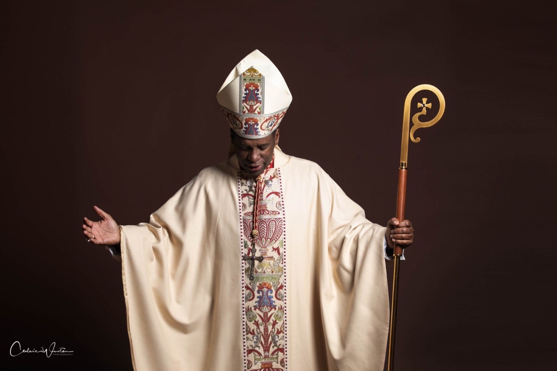 Bishop H. Curtis Douglas in cream episcopal vestments and mitre, holding a crozier, with one hand extended.